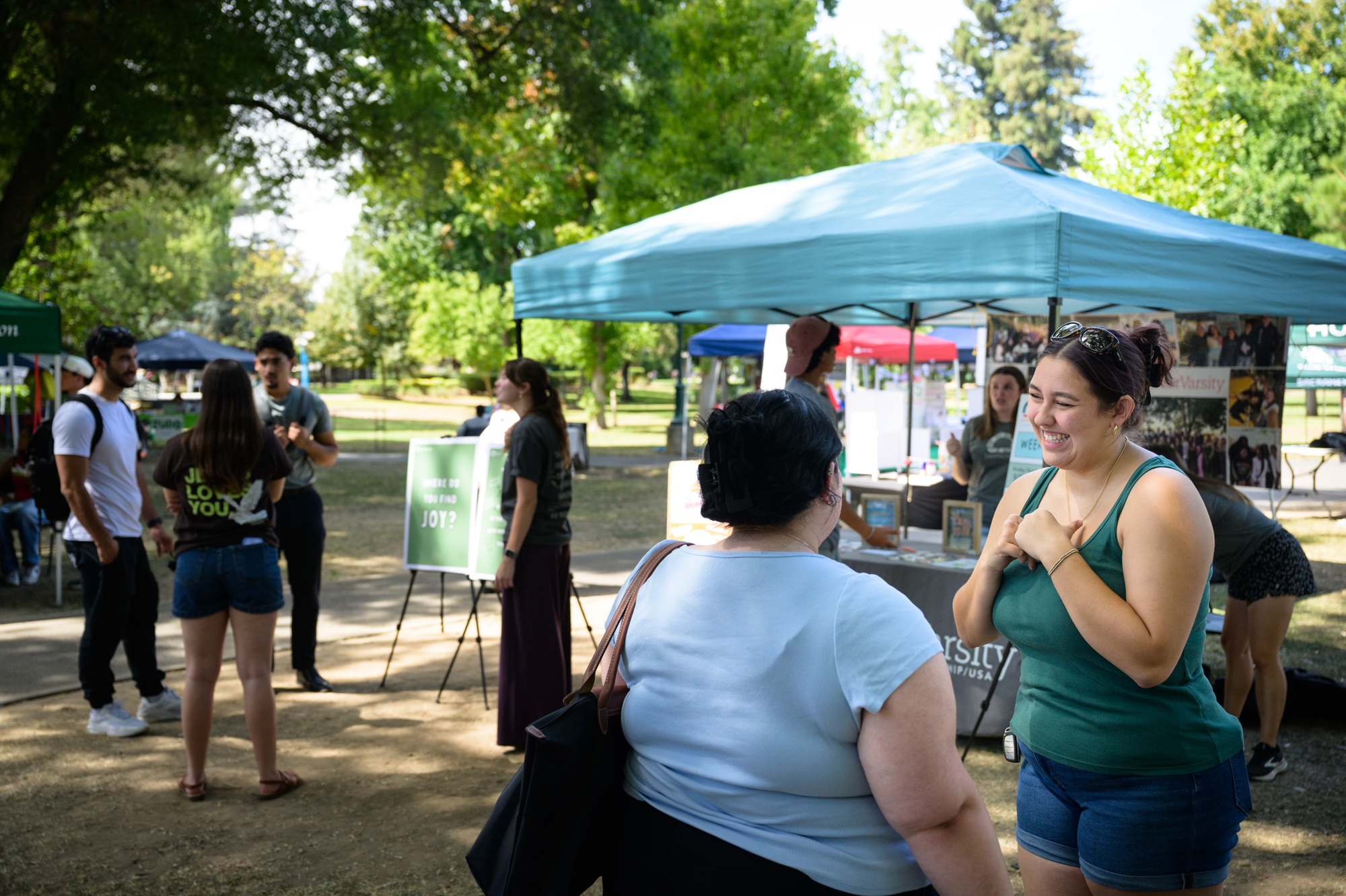 An InterVarsity student smiles as she interacts with another student in front of the table. Other conversations can be seen happening in the background. 