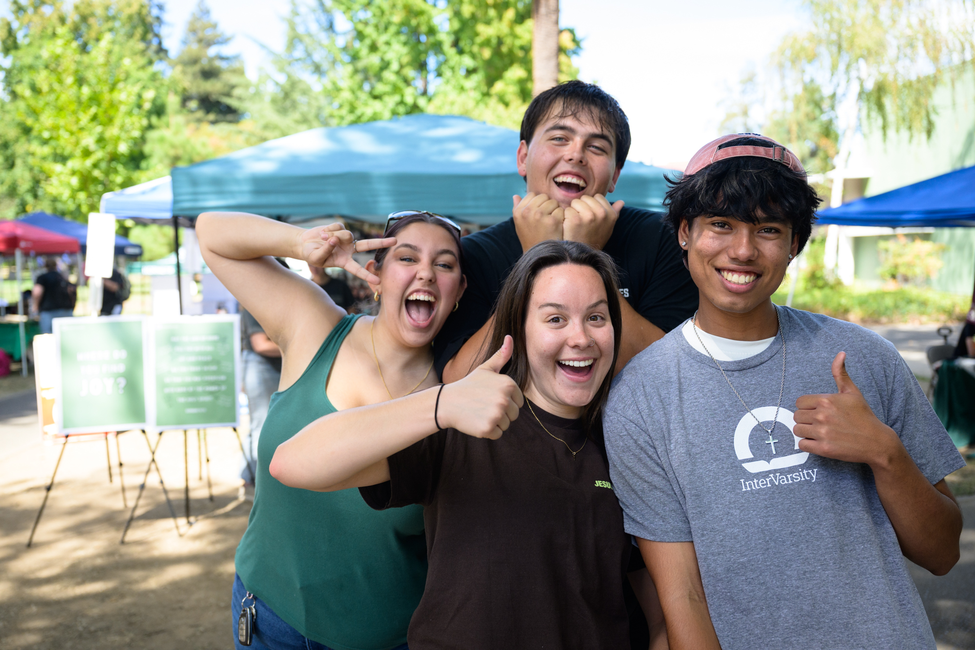 Four students pose in front of the InterVarsity table with happy and silly expressions, ready for a day of connecting with others.