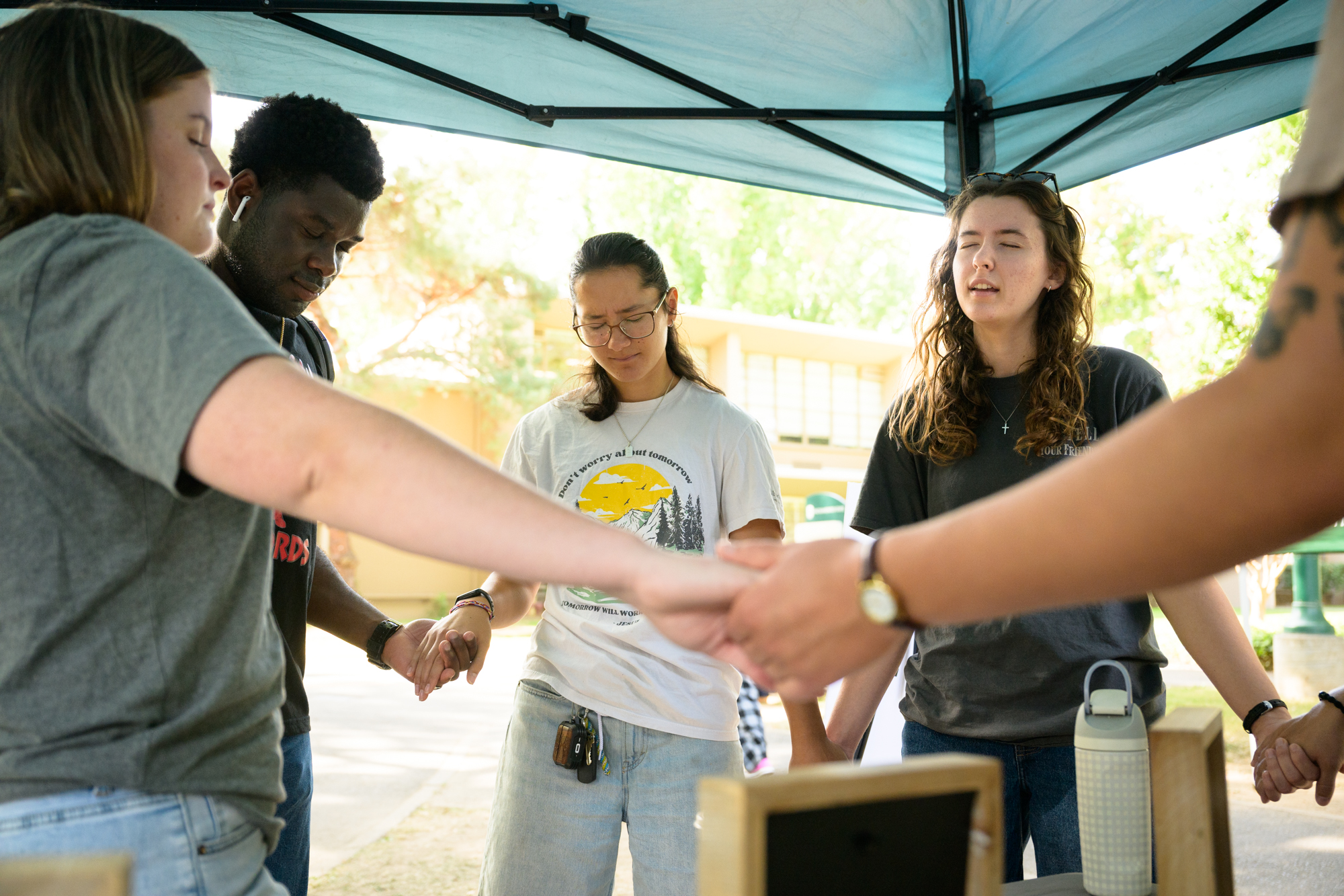 Students stand hand in hand praying in front of the table before they start having conversations.