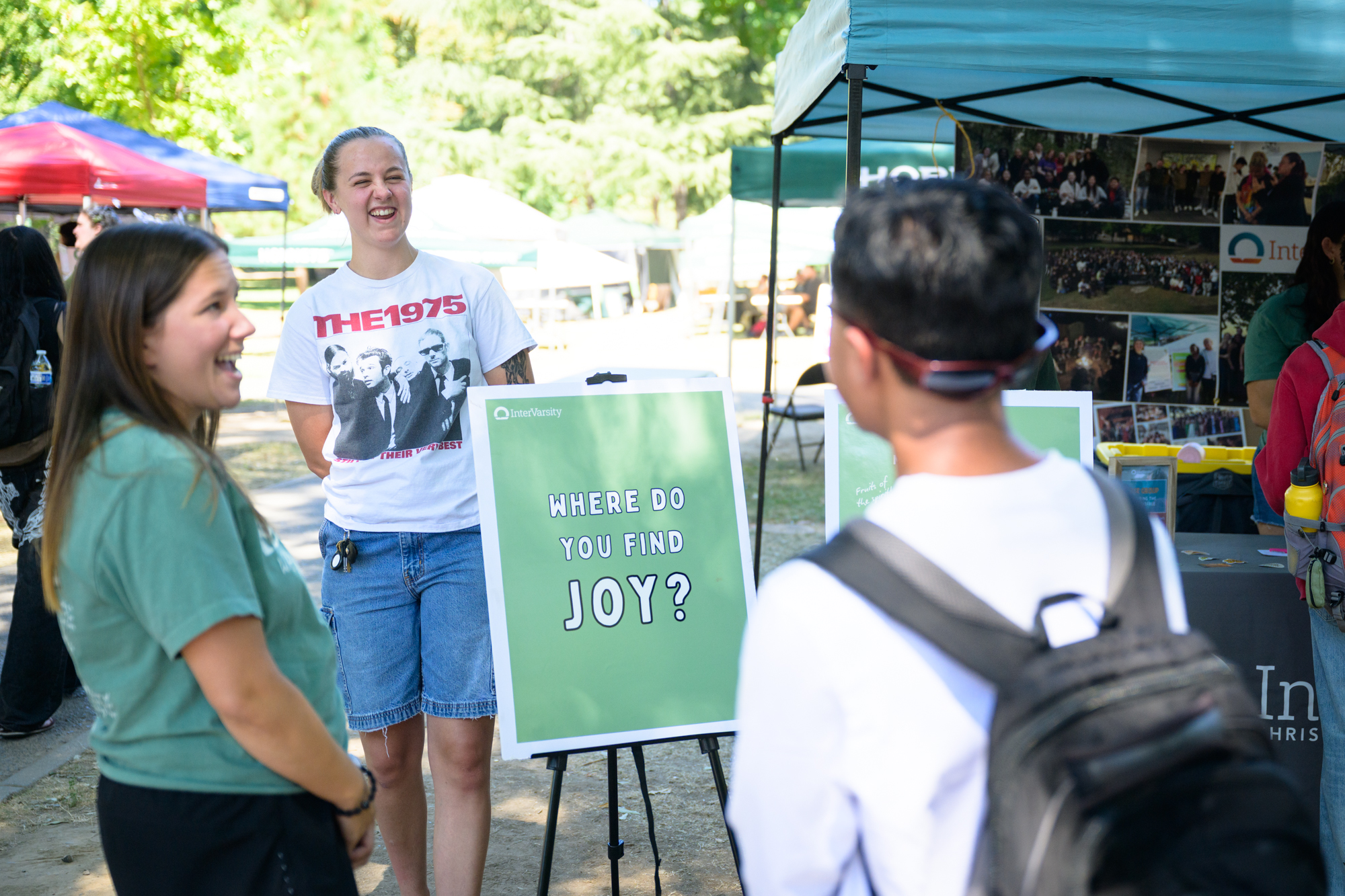 Students and staff laugh at the InterVarsity table while talking with others. They stand near a sign that asks, “Where do you find joy?”