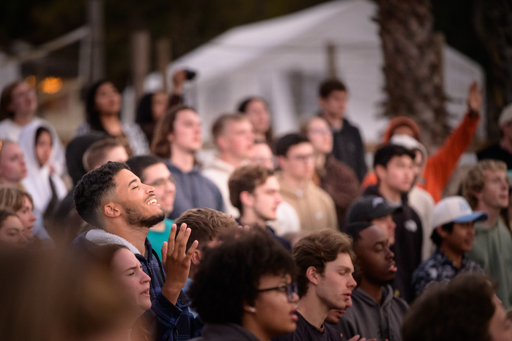 the camera focuses on one student worshipping in the crowd with smile on his face and a hand lifted up.