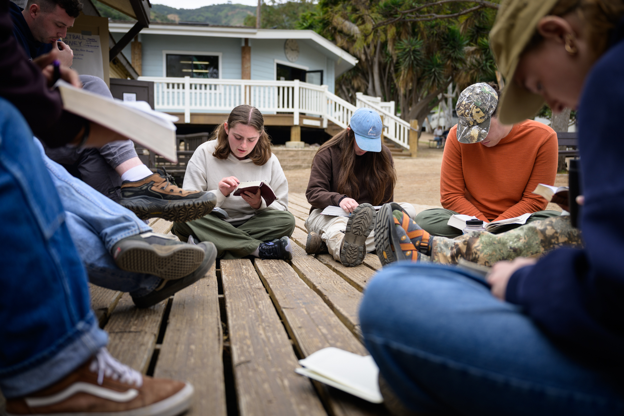 students sit on the ground outside their meeting hall as they read through the Bible together