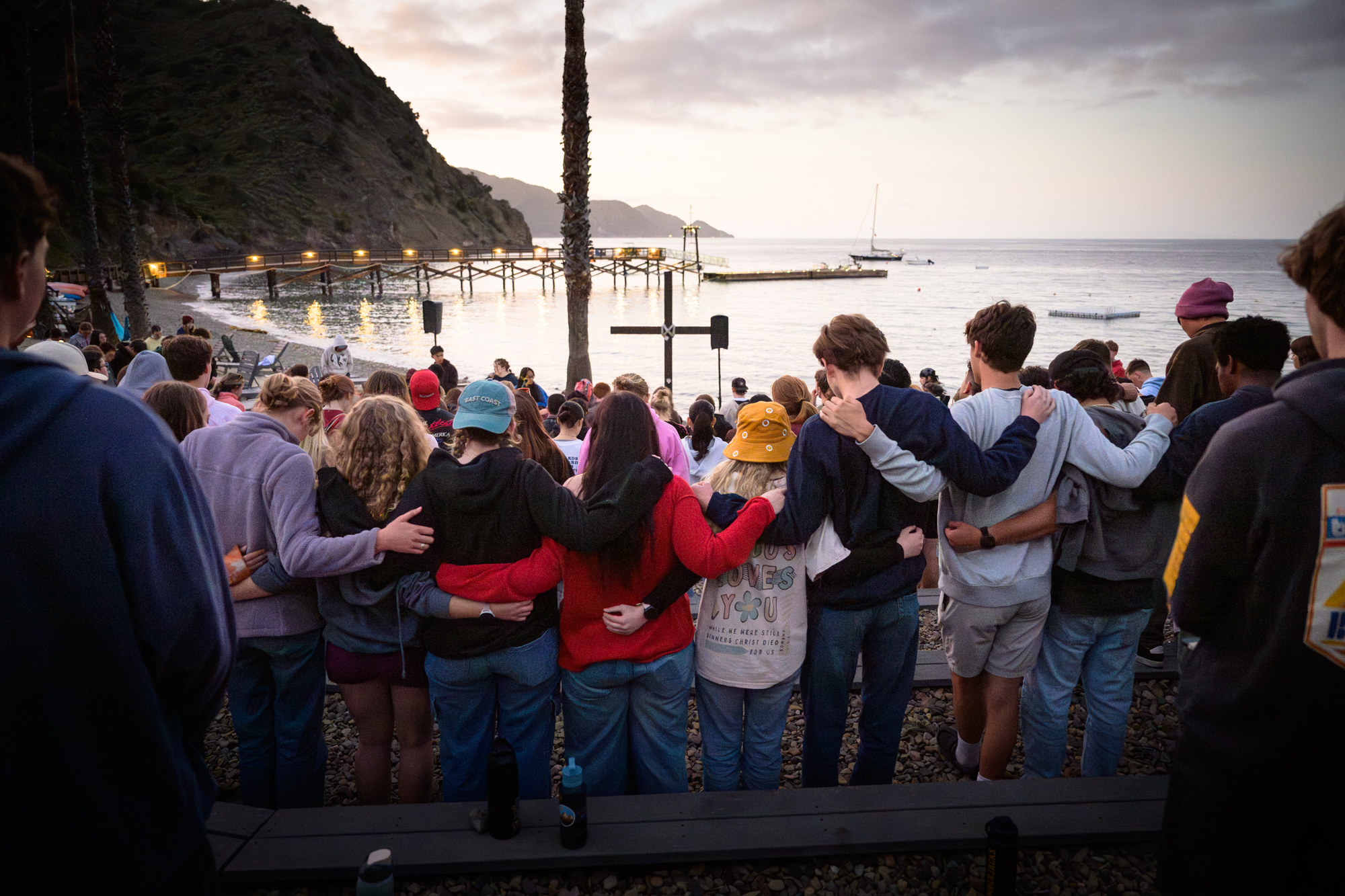 a row of students link arms in the amphitheater as they worship at sunset.