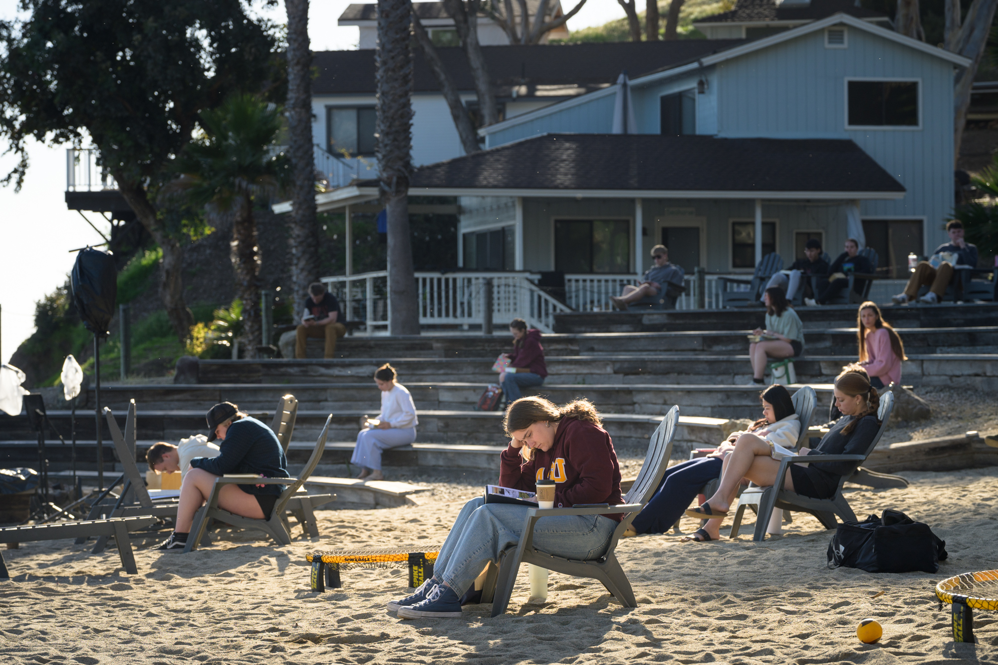 16 students sitting on the sand facing the ocean having quiet time