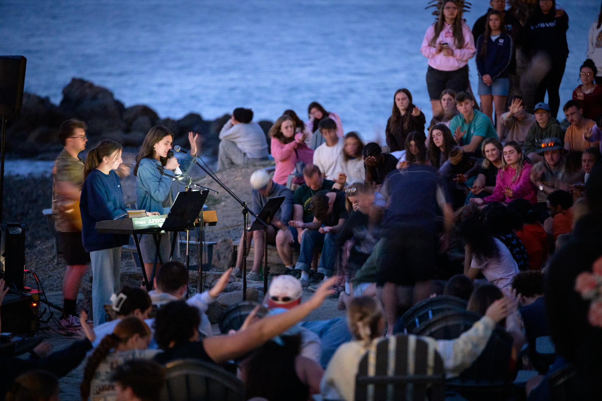 staff worker prays over students in the crowd after worship with ocean in the background