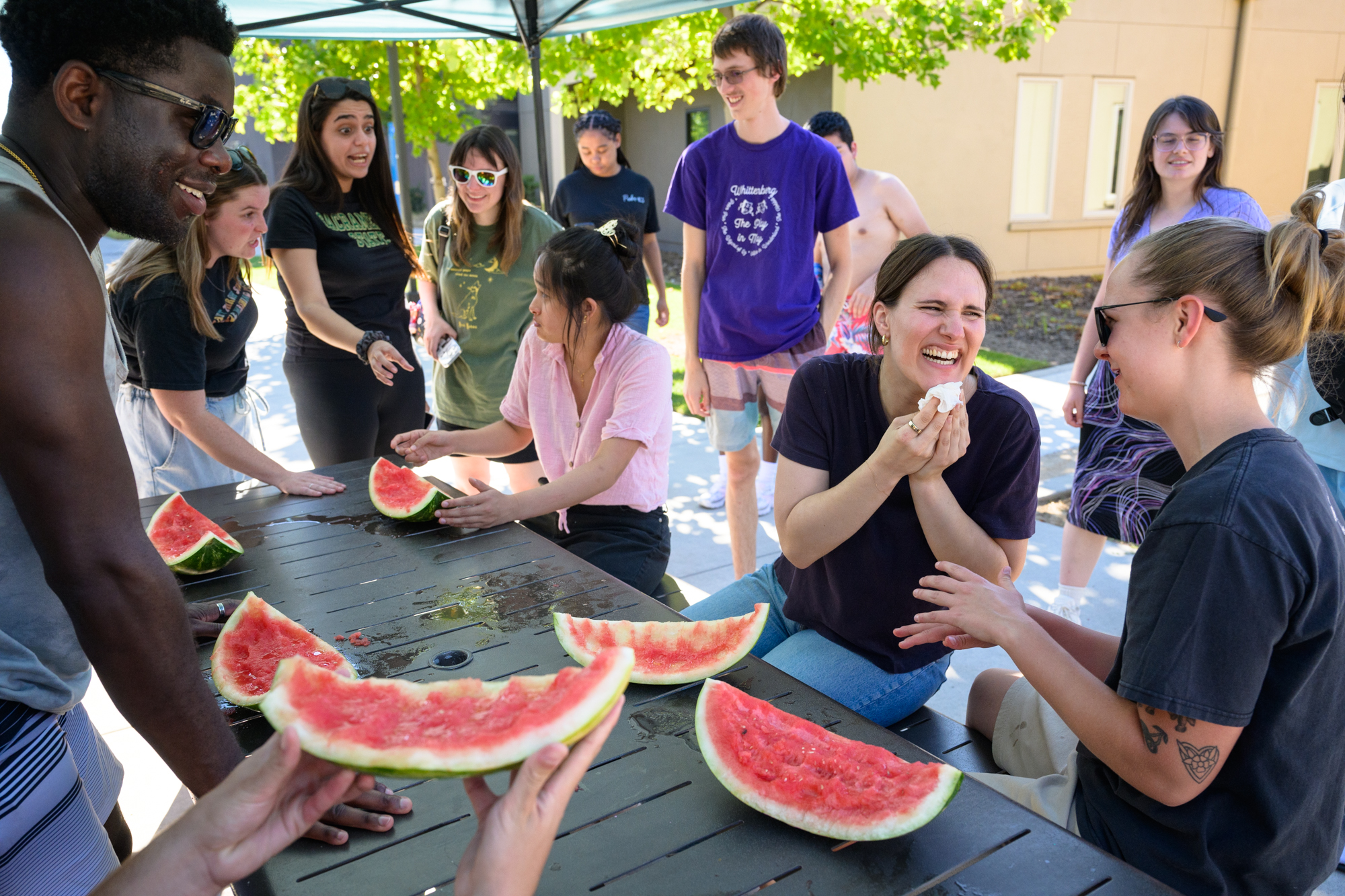Two students look at each other and laugh after the watermelon eating contest, wiping their mouth with a napkin as their eaten watermelon rinds sit in front of them on the table.