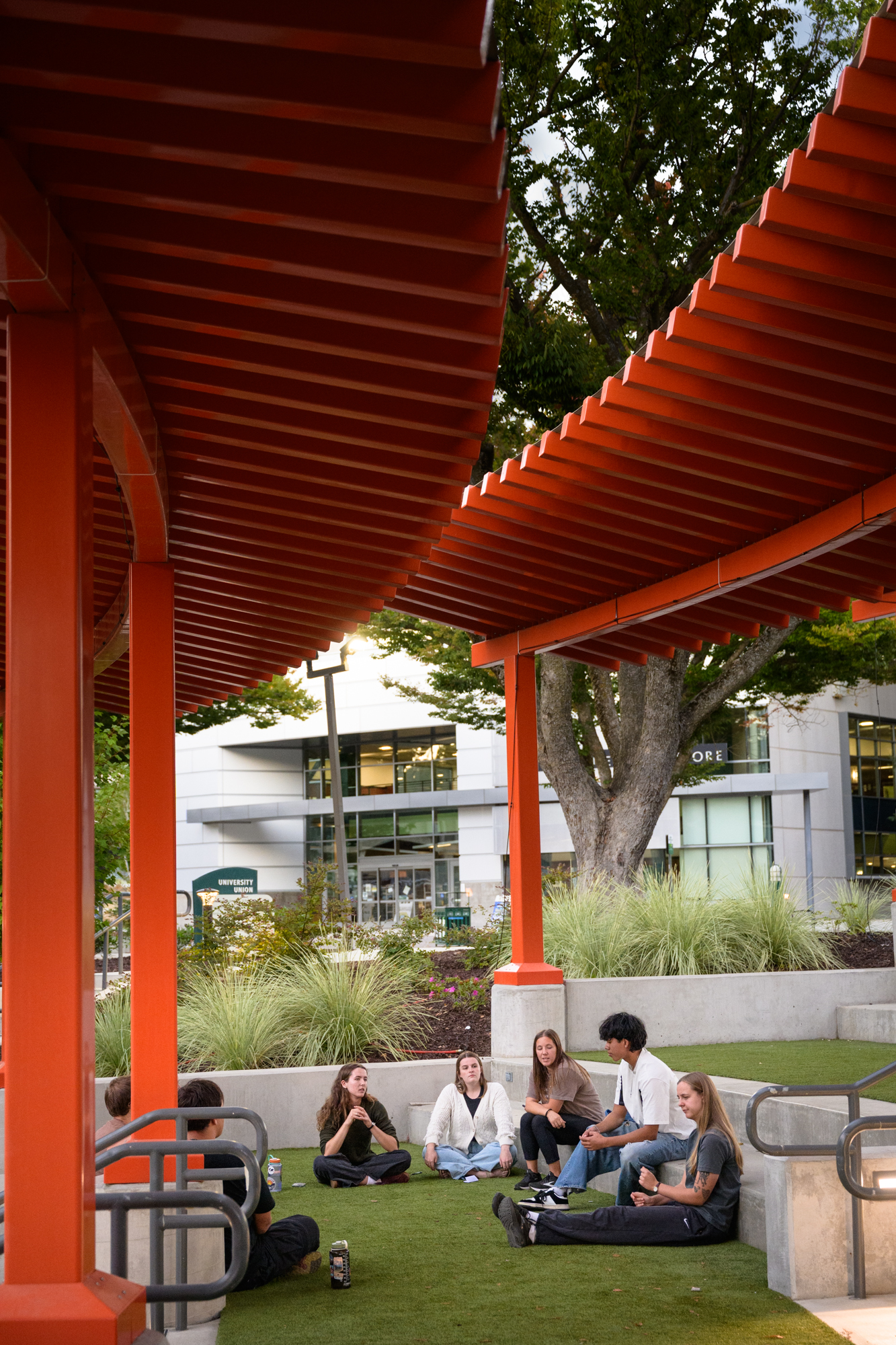 Students sit on the ground under red canopies on campus.