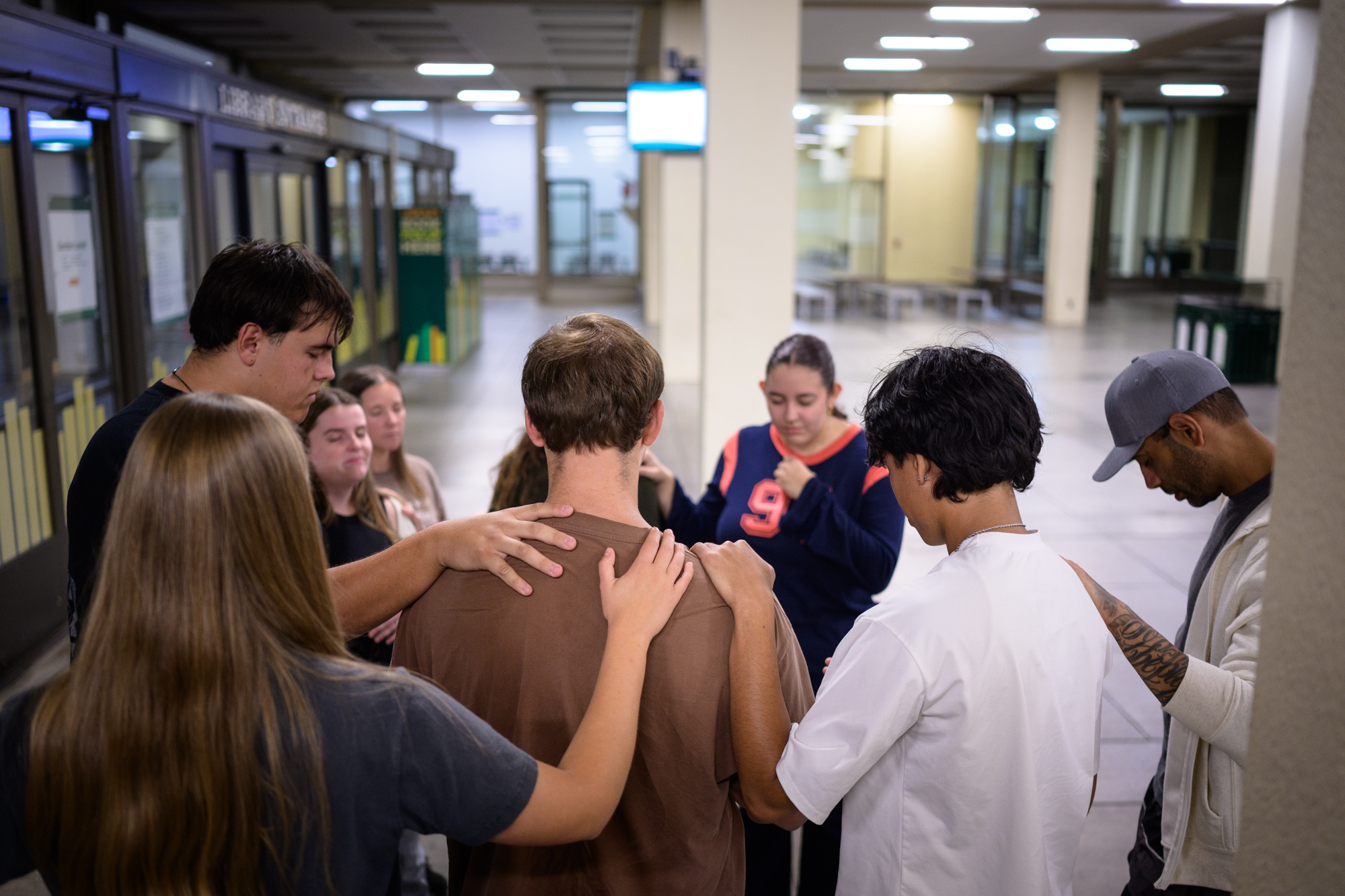 Students lay hands on another student as they huddle in prayer outside the library on campus.