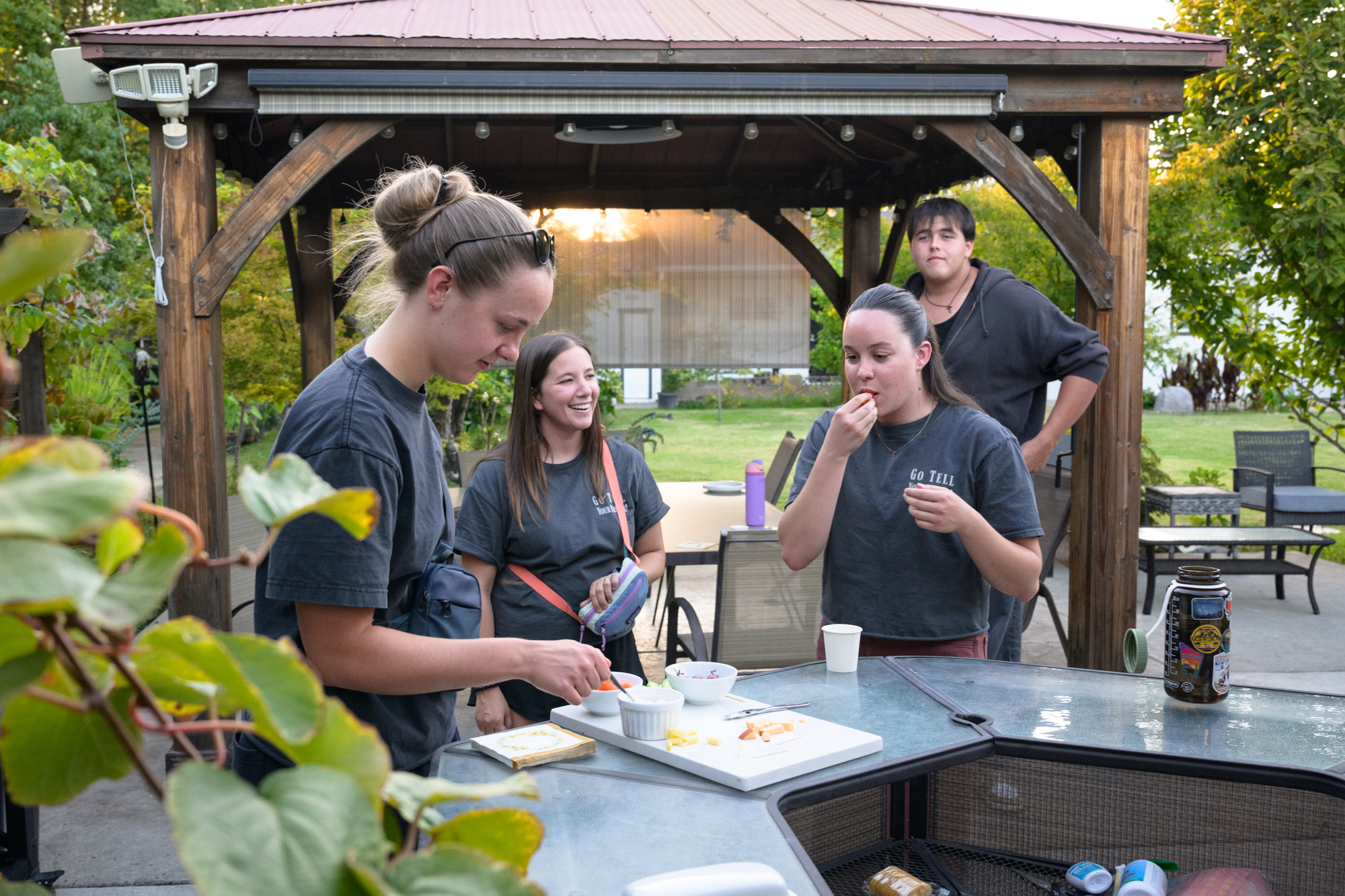 Students stand outside near a tall table, snacking on cheese and crackers.