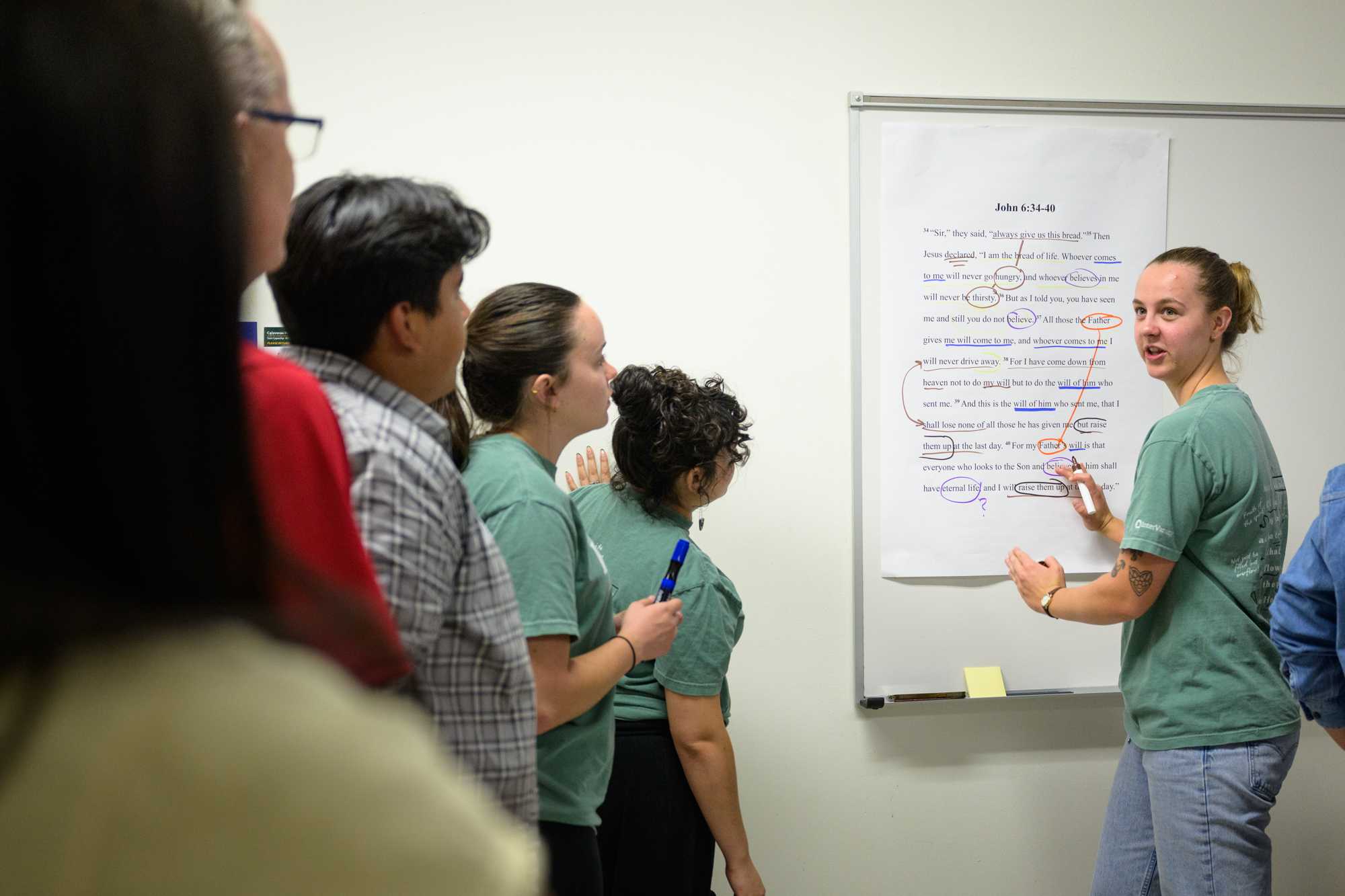 Clair points to a section of text on a large printout of John 6:34-40; many words are circled and lines connect ideas.