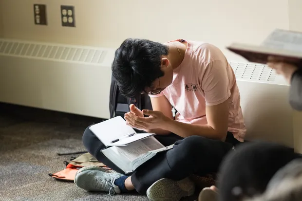 student sitting on floor, reading bible and taking notes