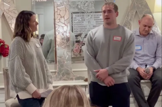 Man standing and speaking with a woman and a man sitting behind him