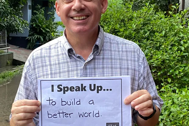Man smiling and holding a sign that says "I speak up...to build a better world"