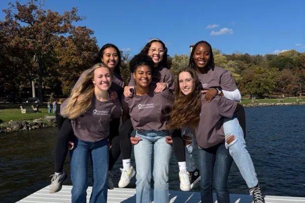 group of female students smiling for a photo by the lake