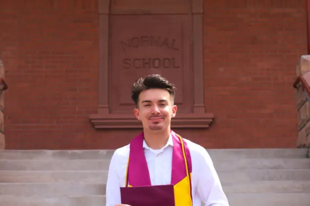 Joseph holding his diploma outside in front of a building