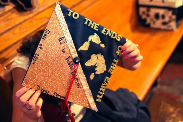 hands holding a graduation cap that reads "To the ends of the earth" on top