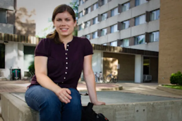 a female student sitting on a fountain in front of a dormitory building