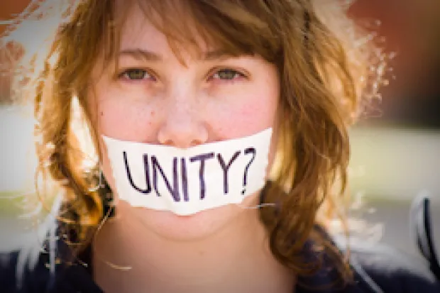 Closeup of woman with paper over mouth with the word: Unity?