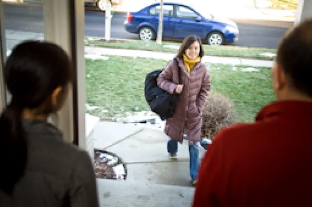 Student walking up the sidewalk to greet parents standing in the doorway