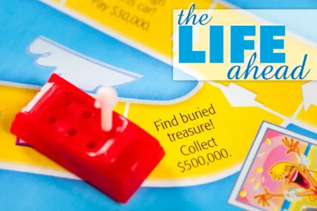 A plastic red car on the board from the board game "Life", and the words "The Life Ahead"