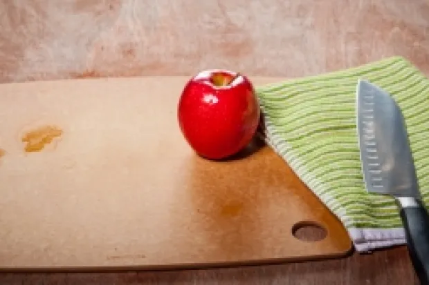 Red apple on cutting board next to kitchen knife on towel