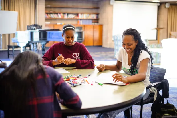 Three students gathered at table doing manuscript Bible study with pile of colored pencils and marked up manuscript sheets