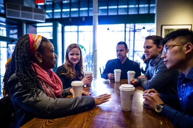 A group of students gathered around a table, drinking coffee, and talking