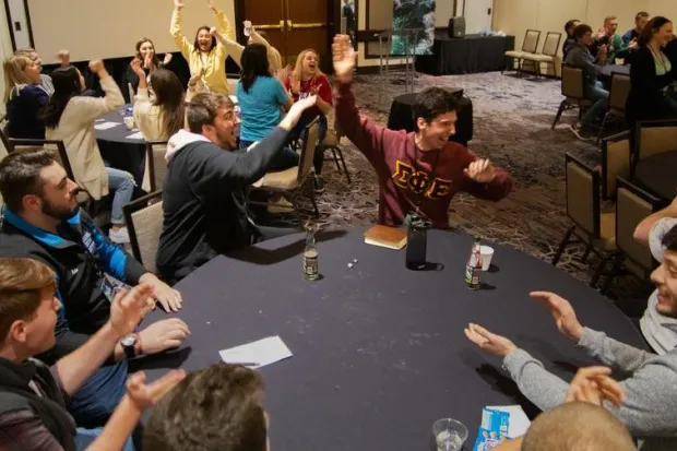 Group of students playing game at tables, cheering and smiling