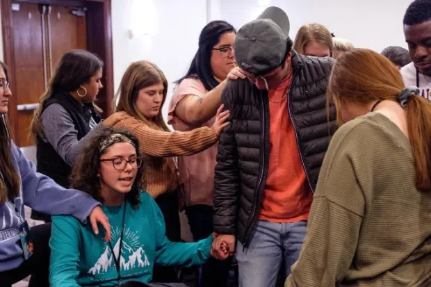 Group of students gathered around praying over another student