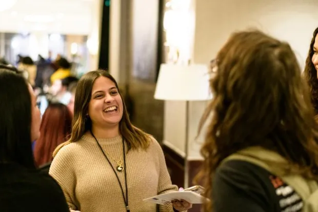 Group of four women talking and laughing in hotel hallway outside of conference session