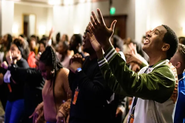 Group of students at conference worshiping, raising hands and singing