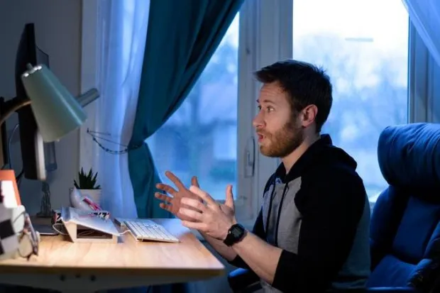 Young male staff sitting at desk having Zoom call on laptop