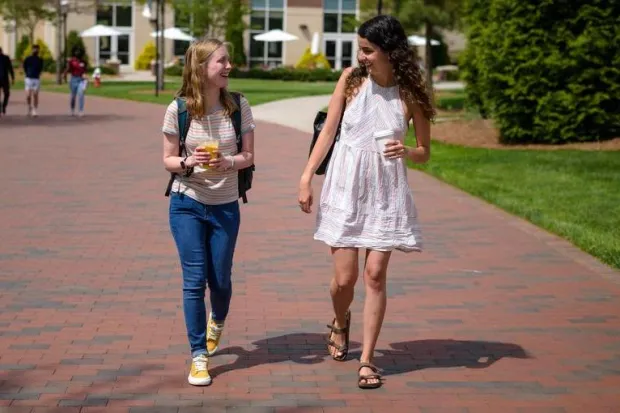 Campus minister Liv Brazer on campus walking down sidewalk talking to female student 