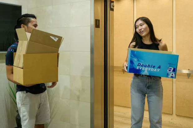 Two students moving into dorm, holding cardboard boxes