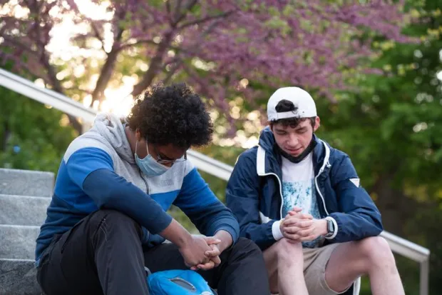 Two men praying together on the steps outside of campus building