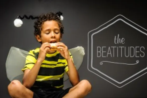 Young boy in bee costume sitting, eating sandwich with the words "The Beatitudes" in the background.