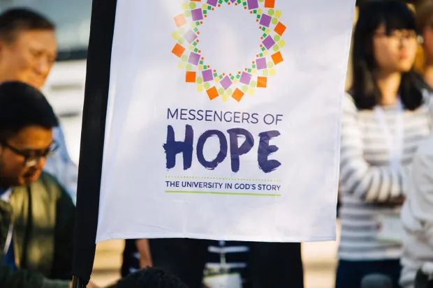 A white sign reading "Messengers of Hope: The University in God's Story"