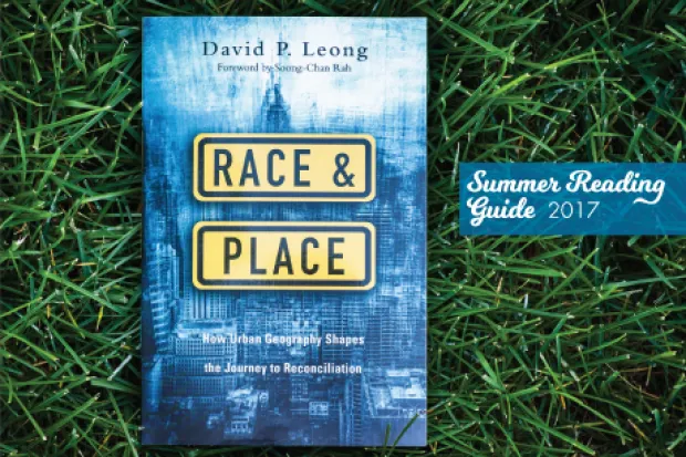 Book cover of Race & Place (blue image of cityscape) laid out on the grass with label: Summer Reading Guide 2017