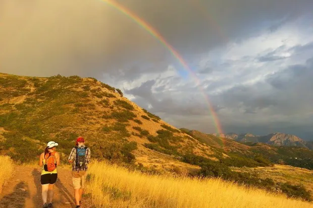 Two people hiking up a trail with cloudy sky and rainbow