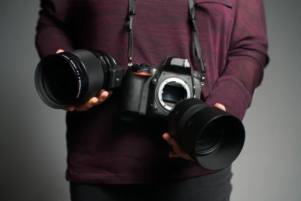 Two hands holding a camera and changing its lenses