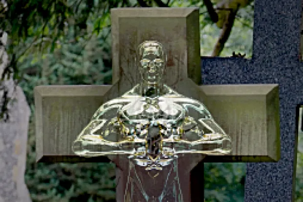 A gold statue standing perfectly in line with a wooden cross right behind it.