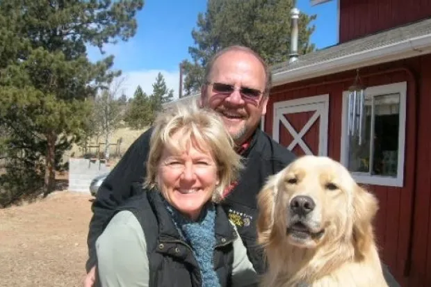 a man, woman, and dog smiling in front of a red barn