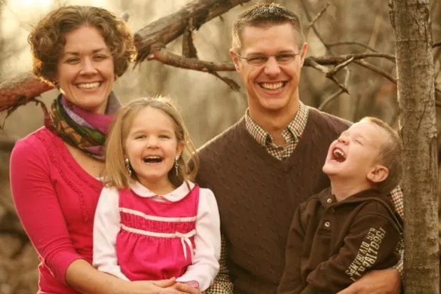 Family photo of mother and father with two small children laughing