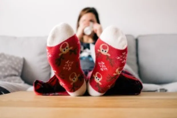 Woman sitting on couch wearing red Christmas socks propped up on table holding mug