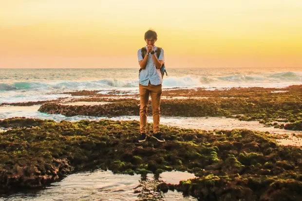 Young man standing beside tide pool at sunset