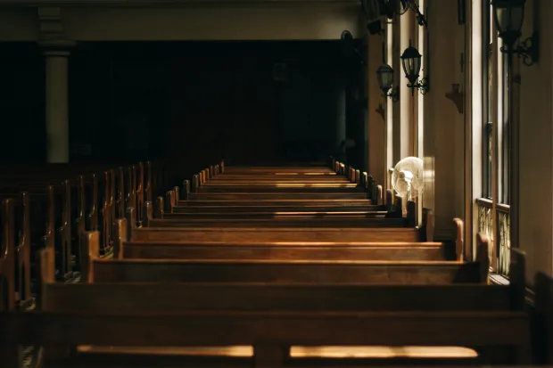 a brown wooden church bench near a white painted wall