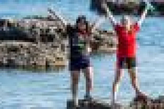 Two young women standing at the edge of the water with their arms thrown up in the air