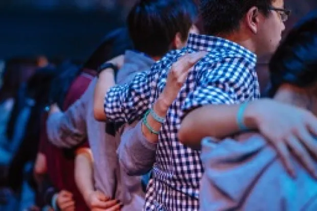 Group of people in auditorium standing with arms around each other