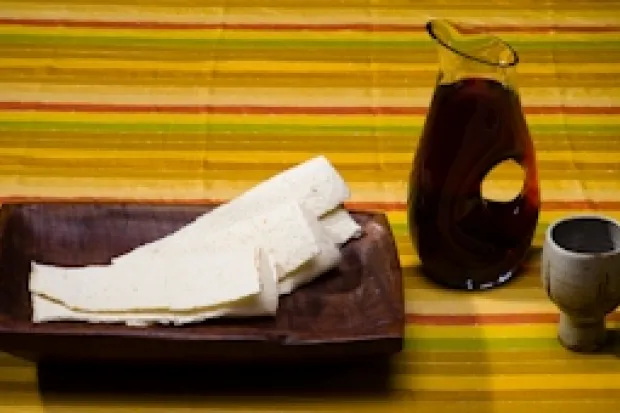 Communion elements on table: strips of flatbread on a wooden plate, a pitcher of juice, and a plain ceramic cup