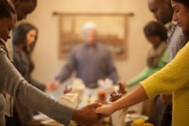 people of different ethnicities holding hands and praying across a dinner table